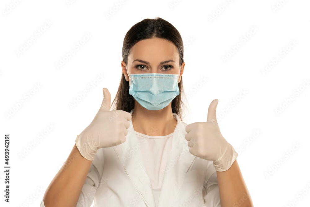 Beautiful female doctor or nurse wearing protective mask and latex or rubber gloves on white background with thumbs up. Beautiful female doctor or nurse wearing protective mask and latex or rubber gloves on white background with thumbs up.