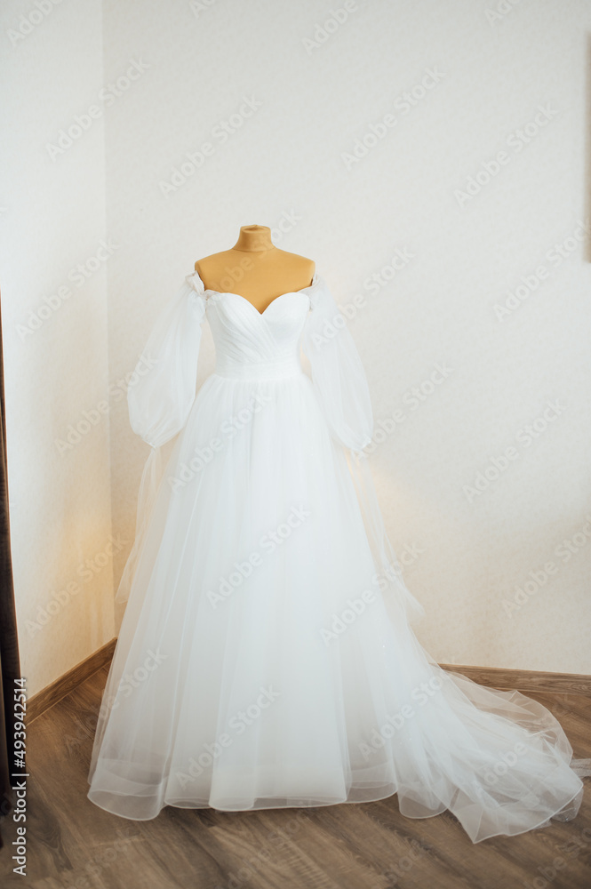 The bride's dress hangs on the window. A gentle bouquet of the bride and women's shoes stand on the windowsill The bride's dress hangs on the window. A gentle bouquet of the bride and women's shoes stand on the windowsill