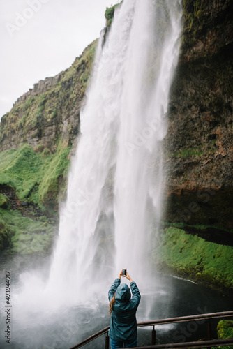 Girl taking a picture of Iceland Seljalandsfoss waterfall. No face, shot from the back