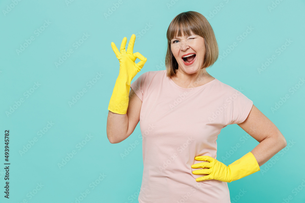 Elderly satisfied housewife woman 40s in pink t-shirt gloves doing housework showing okay ok gesture wink isolated on plain pastel light blue background studio Housekeeping cleaning tidying up concept Elderly satisfied housewife woman 40s in pink t-shirt gloves doing housework showing okay ok gesture wink isolated on plain pastel light blue background studio Housekeeping cleaning tidying up concept