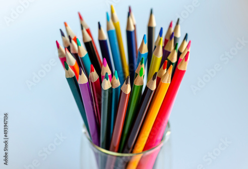 Multi-colored pencils in a transparent glass close-up on a light background. The concept of creativity, drawing. 