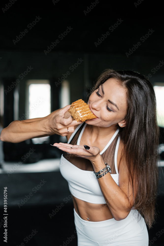 Attractive woman in white sportswear is eating delicious dessert. Sexy girl doing workout in gym. Diet and fitness concept. Attractive woman in white sportswear is eating delicious dessert. Sexy girl doing workout in gym. Diet and fitness concept.