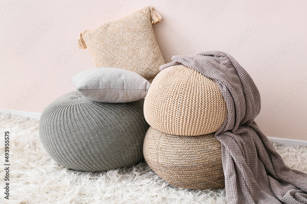 Modern poufs with pillows near light wall in room