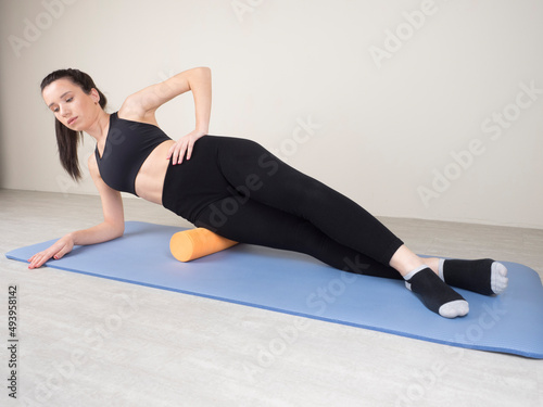 a European girl is engaged in Fitness on her side. cool down after workout. self-massage of leg and thigh muscles on a massage roller.