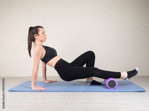 European girl is engaged in fitness on the mat. cool down after exercise. self-massage of the muscles of the calves of the legs on a massage roller. static load and home gymnastics.