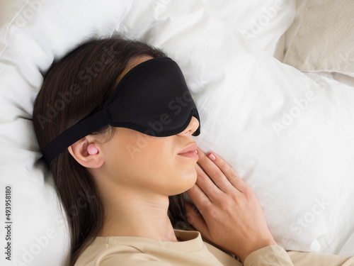 European girl getting ready for bed. a pink ear plug and a sleep mask for complete darkness, peace and quiet all night long. woman on a pillow in the bedroom. healthy lifestyle.