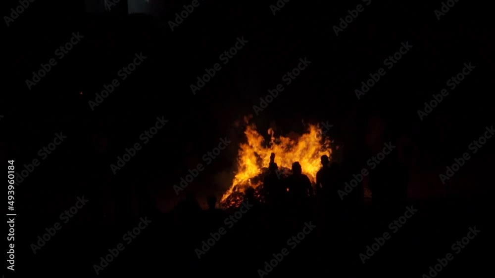 Slow motion shot of large bonfire during the Holi or Holika Dahan festival in India. Silhouette of people visible watching the bonfire at lohri festival. People enjoying lohri in India. Slow motion shot of large bonfire during the Holi or Holika Dahan festival in India. Silhouette of people visible watching the bonfire at lohri festival. People enjoying lohri in India.
