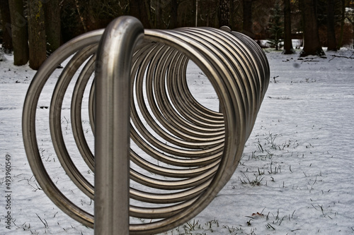 Spiralny stojak , na rowery , ze stali nierdzewnej na trawniku zimą na tle śniegu .