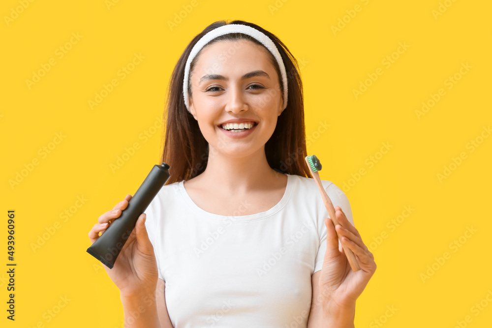 Beautiful young woman with activated charcoal tooth paste and brush on yellow background Beautiful young woman with activated charcoal tooth paste and brush on yellow background