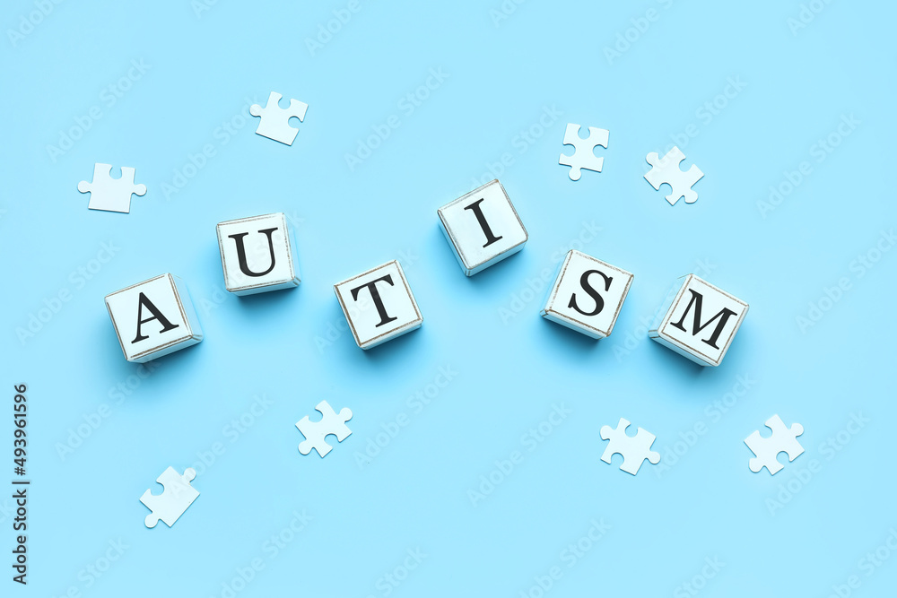 Cubes with word AUTISM and puzzle pieces on blue background Cubes with word AUTISM and puzzle pieces on blue background