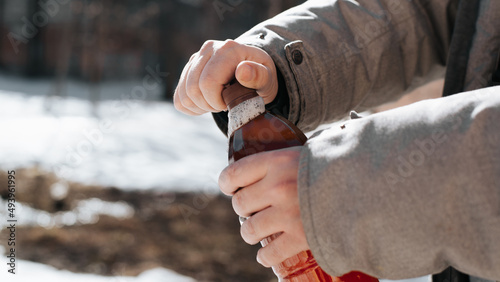 Male hand opening plastic bottle of beer with leaking foam, outdoors. Close-up, side view