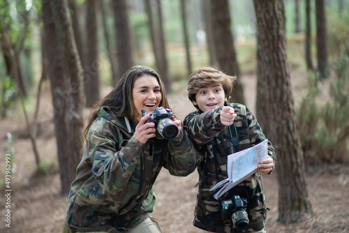 Surprised mother and son taking pictures in forest. Family with modern cameras pointing, looking with wide open eyes. Parenting, family, leisure concept