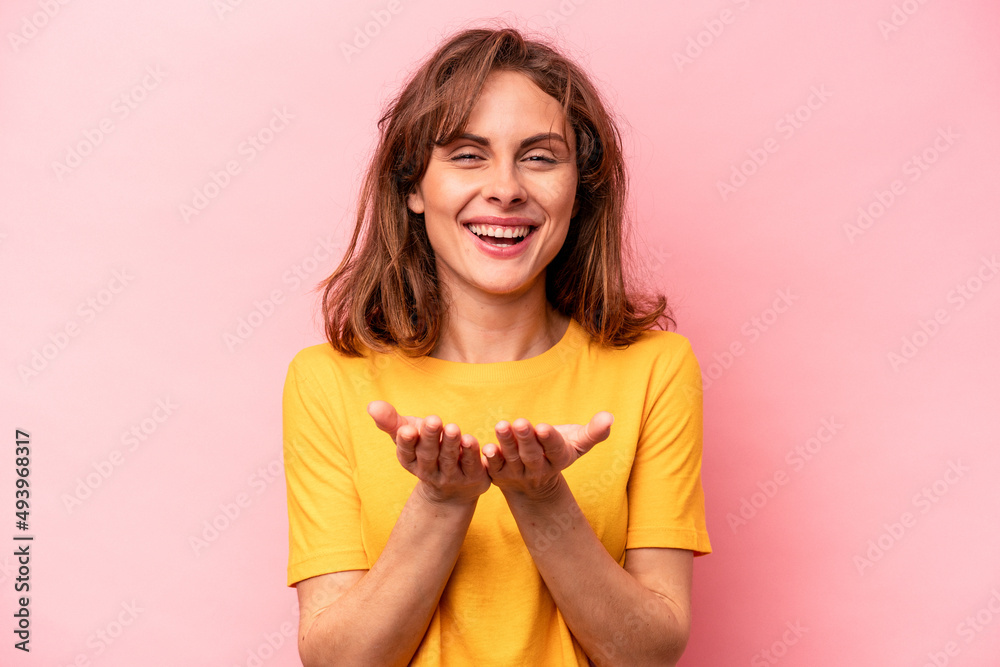 Young caucasian woman isolated on pink background holding something with palms, offering to camera. Young caucasian woman isolated on pink background holding something with palms, offering to camera.