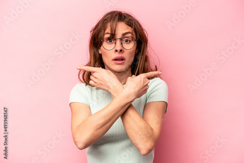 Young caucasian woman isolated on pink background points sideways, is trying to choose between two options.