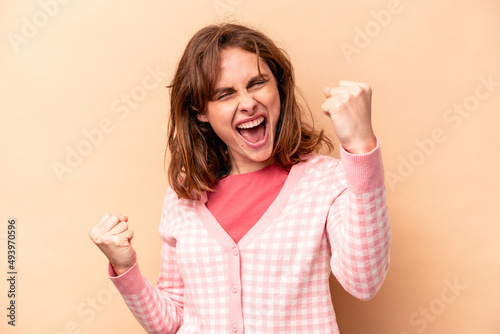 Young caucasian woman isolated on beige background cheering carefree and excited. Victory concept. © Asier