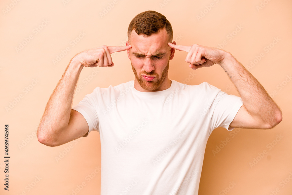 Young caucasian man isolated on beige background focused on a task, keeping forefingers pointing head.
