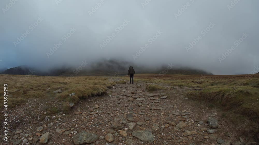 A man with large backpack walking a gravel trail in the mountain fog and mist A man with large backpack walking a gravel trail in the mountain fog and mist
