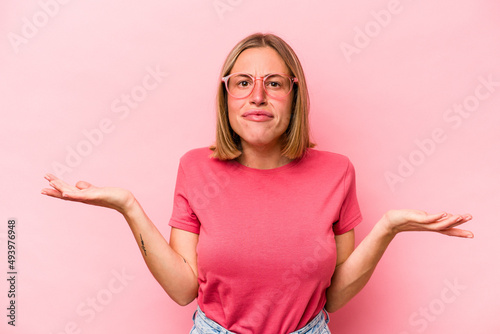 Young caucasian woman isolated on pink background doubting and shrugging shoulders in questioning gesture.