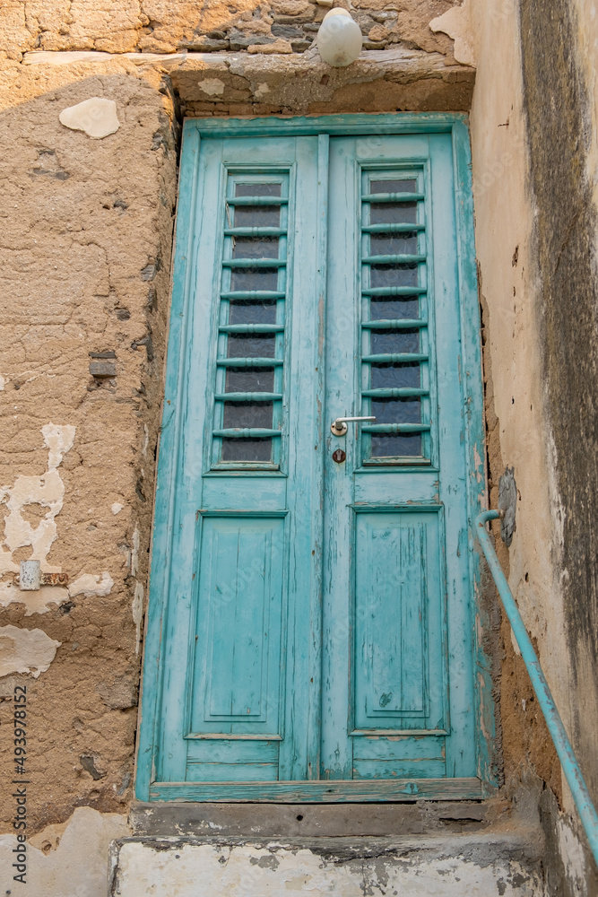 Greek Island, Cyclades. Building with peeled wall, blue wooden close aged door. Under view. Vertical