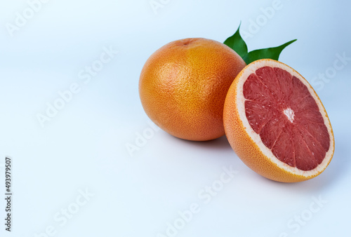 a whole grapefruit and a half with green leaves on a white background