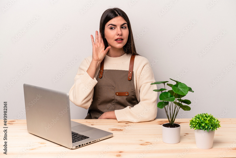 Young caucasian gardener woman working on the table isolated on pink background trying to listening a gossip. Young caucasian gardener woman working on the table isolated on pink background trying to listening a gossip.