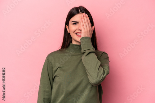 Young caucasian woman isolated on pink background having fun covering half of face with palm. © Asier