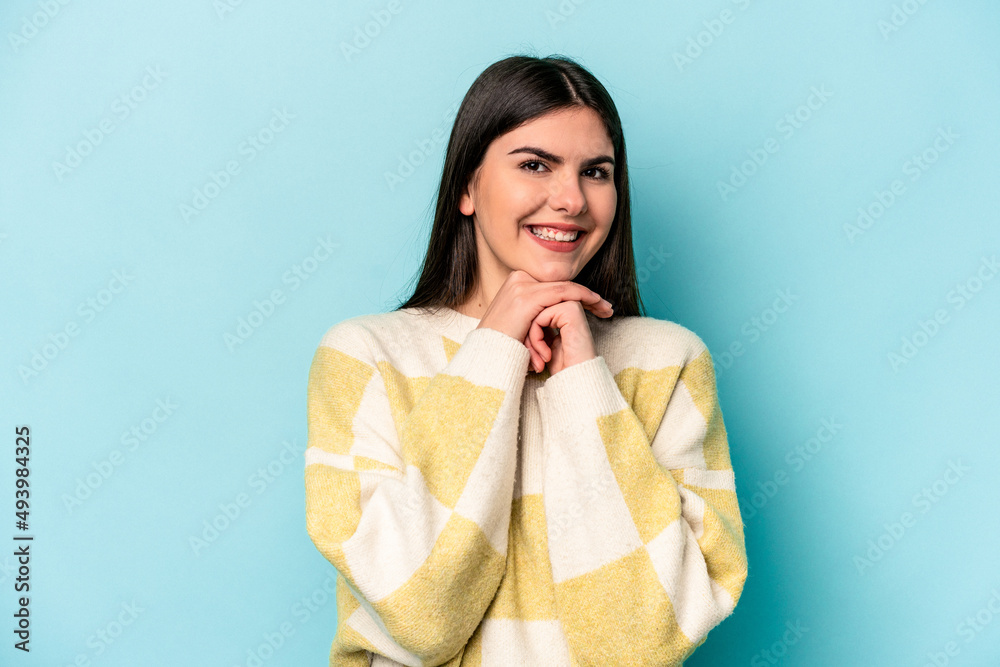 Young caucasian woman isolated on blue background keeps hands under chin, is looking happily aside. Young caucasian woman isolated on blue background keeps hands under chin, is looking happily aside.