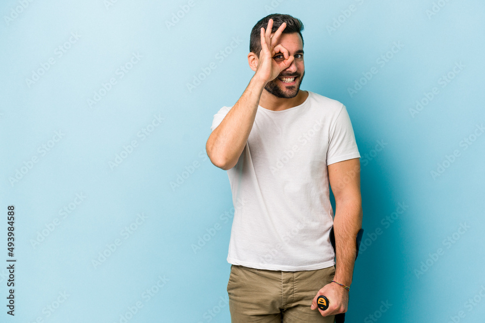Young man with crutches isolated on blue background excited keeping ok gesture on eye. Young man with crutches isolated on blue background excited keeping ok gesture on eye.