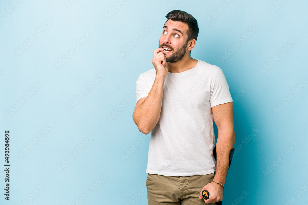 Young man with crutches isolated on blue background relaxed thinking about something looking at a copy space. Young man with crutches isolated on blue background relaxed thinking about something looking at a copy space.