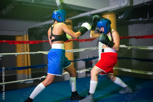 Sporty female boxers boxing in gym. Two trained girls in helmets and gloves practicing sparring on ring, attacking each other making blows, learning to defend. Healthy lifestyle, extreme sport concept © KAMPUS
