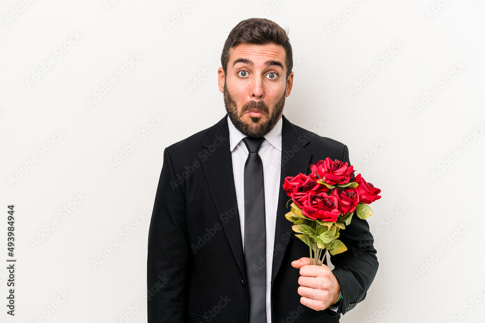 Young caucasian man holding a bouquet of flowers isolated on white background shrugs shoulders and open eyes confused. Young caucasian man holding a bouquet of flowers isolated on white background shrugs shoulders and open eyes confused.