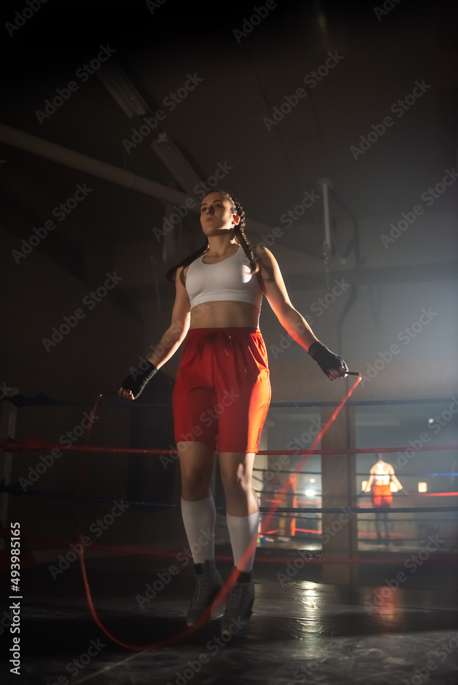 Young girl training with skipping rope in gym. Beautiful Caucasian girl in sportswear using jump rope warming up before exercising boxing. Healthy lifestyle and sport activity concept