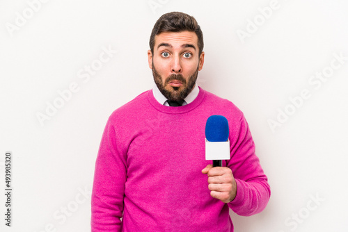 Young caucasian tv presenter man isolated on white background shrugs shoulders and open eyes confused. © Asier