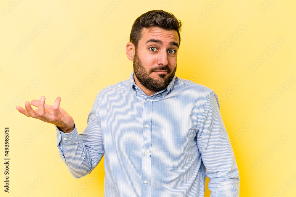 Young caucasian man isolated on yellow background doubting and shrugging shoulders in questioning gesture. Young caucasian man isolated on yellow background doubting and shrugging shoulders in questioning gesture.