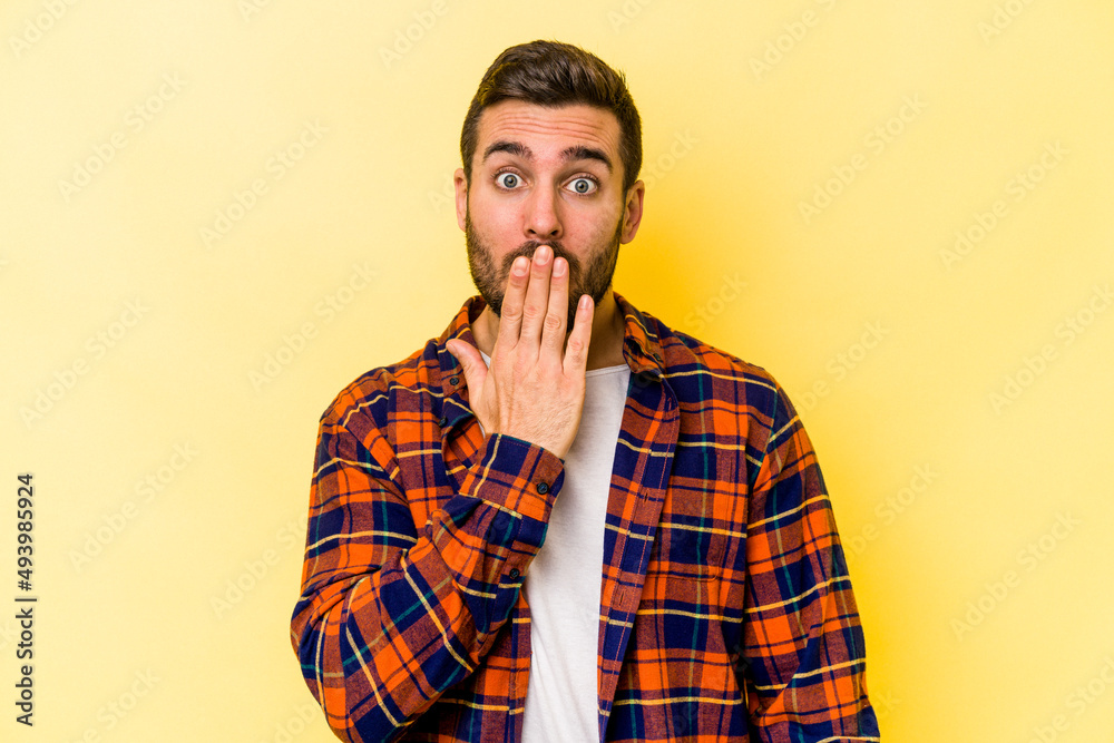 Young caucasian man isolated on yellow background shocked, covering mouth with hands, anxious to discover something new.