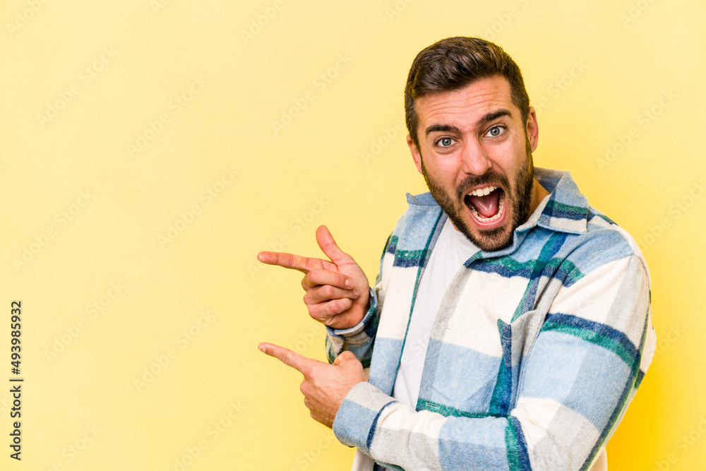 Young caucasian man isolated on yellow background pointing with forefingers to a copy space, expressing excitement and desire. Young caucasian man isolated on yellow background pointing with forefingers to a copy space, expressing excitement and desire.