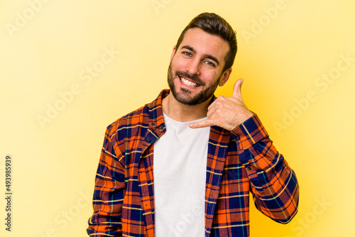 Young caucasian man isolated on yellow background showing a mobile phone call gesture with fingers.