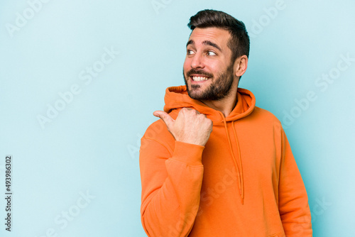 Young caucasian man isolated on blue background points with thumb finger away, laughing and carefree. © Asier