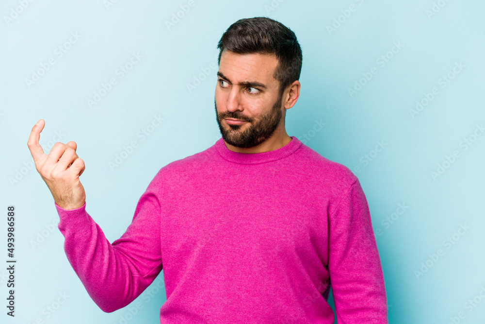 Young caucasian man isolated on blue background pointing with finger at you as if inviting come closer. Young caucasian man isolated on blue background pointing with finger at you as if inviting come closer.