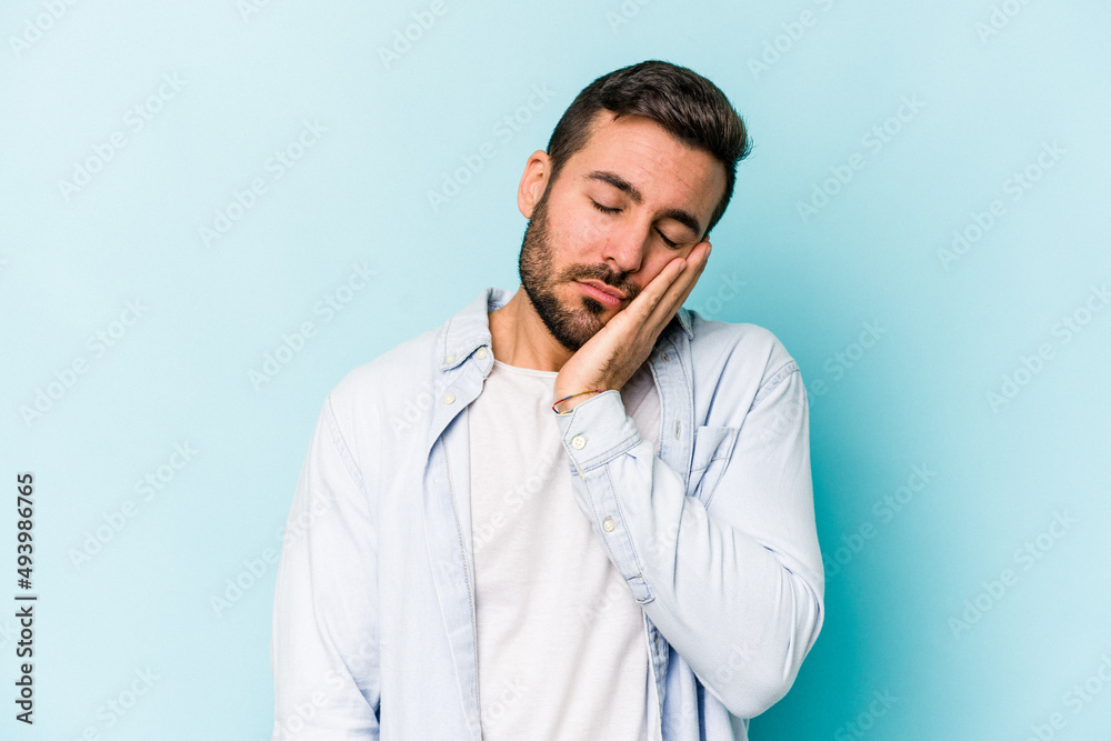 Young caucasian man isolated on blue background who is bored, fatigued and need a relax day. Young caucasian man isolated on blue background who is bored, fatigued and need a relax day.
