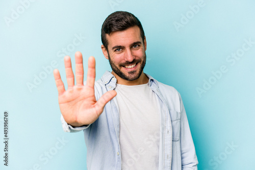 Young caucasian man isolated on blue background smiling cheerful showing number five with fingers. photo