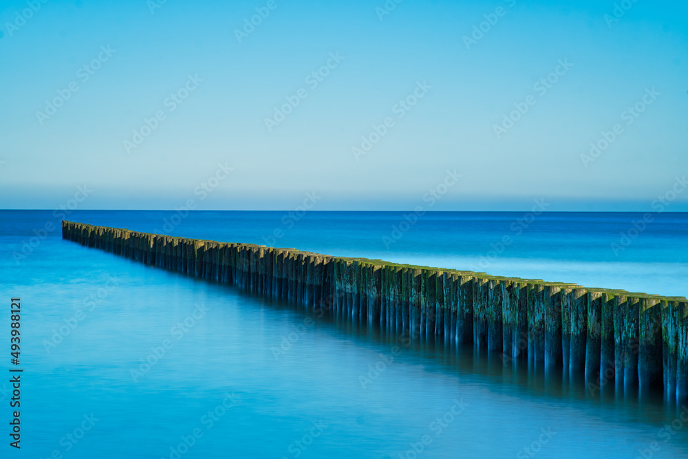 a wooden breakwater at the baltic sea with a blue sky and calm water