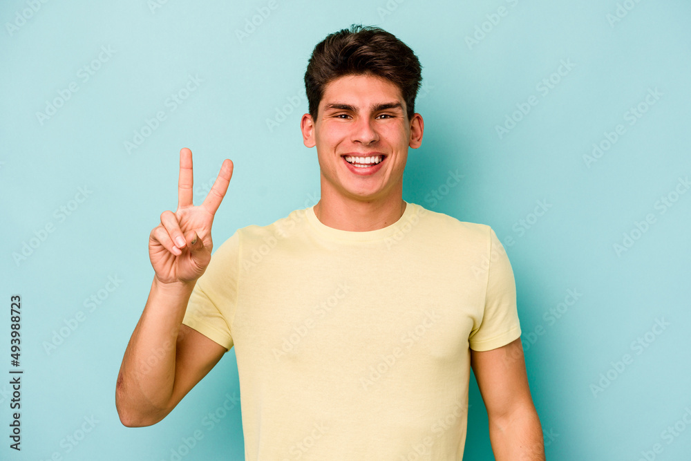 Young caucasian man isolated on blue background joyful and carefree showing a peace symbol with fingers. Young caucasian man isolated on blue background joyful and carefree showing a peace symbol with fingers.