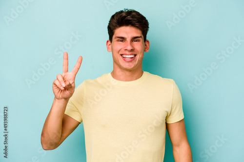 Young caucasian man isolated on blue background joyful and carefree showing a peace symbol with fingers.