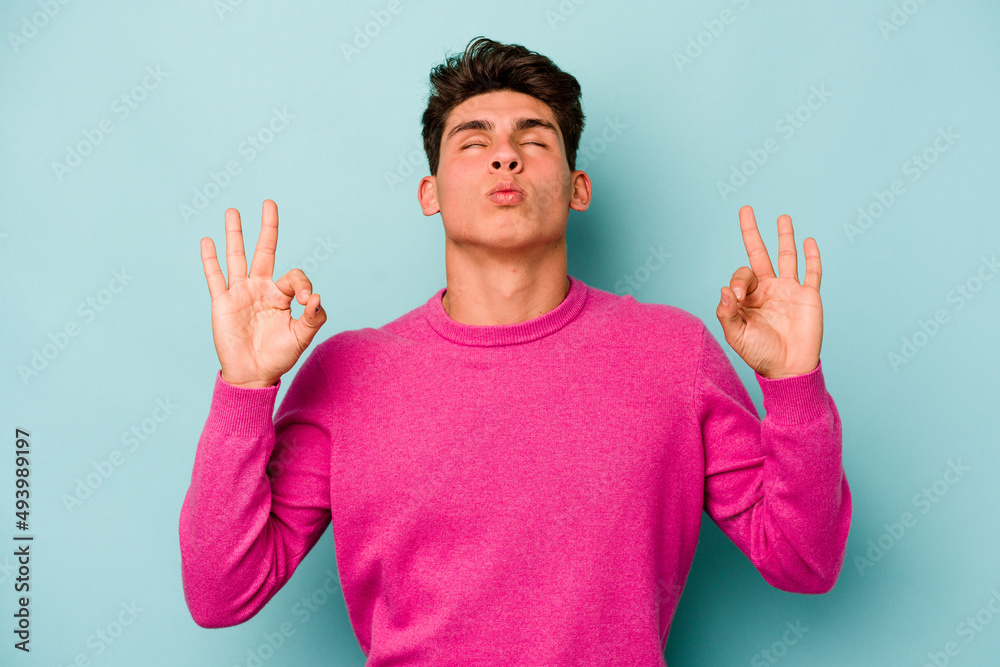Young caucasian man isolated on blue background relaxes after hard working day, she is performing yoga. Young caucasian man isolated on blue background relaxes after hard working day, she is performing yoga.