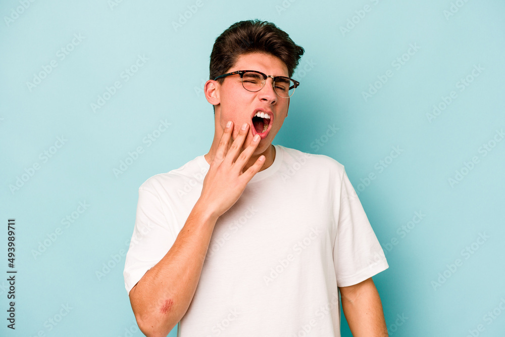 Young caucasian man isolated on blue background yawning showing a tired gesture covering mouth with hand. Young caucasian man isolated on blue background yawning showing a tired gesture covering mouth with hand.