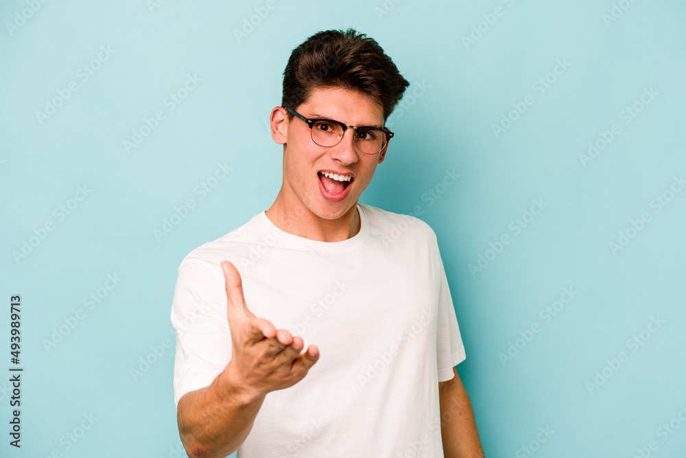 Young caucasian man isolated on blue background stretching hand at camera in greeting gesture. Young caucasian man isolated on blue background stretching hand at camera in greeting gesture.