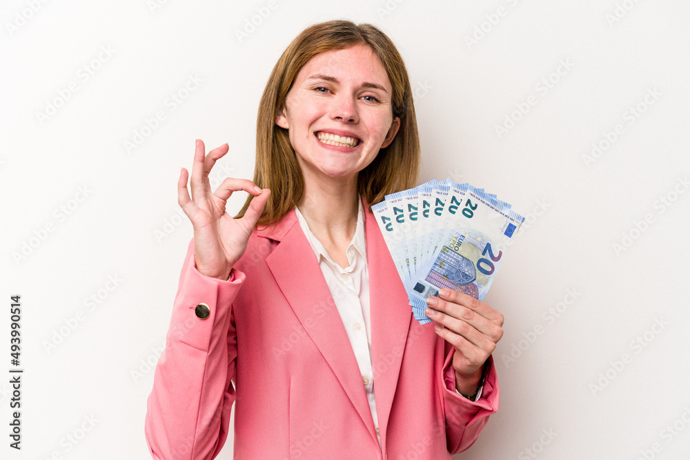 Young business English woman holding banknotes isolated on white background cheerful and confident showing ok gesture. Young business English woman holding banknotes isolated on white background cheerful and confident showing ok gesture.