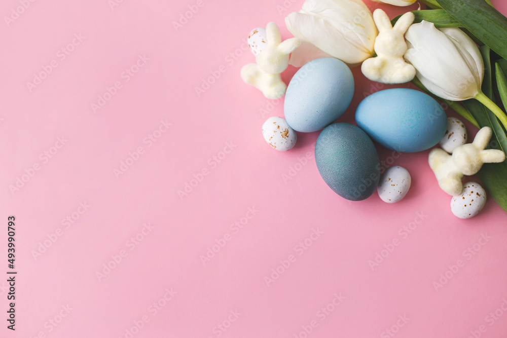 Happy Easter! Easter eggs, tulips and bunnies flat lay on pink background. Modern natural dyed blue easter eggs and white tulips. Greeting card template, with space for text