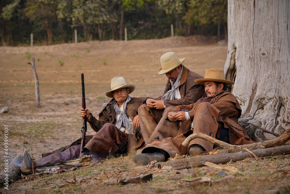 Vintage action shot of a group of cowboys relaxing under a tree. with soft sunlight in the morning